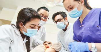 A team of dental professionals in uniforms attends to a patient in a dental clinic setting.