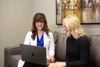 Two women on a couch, collaborating on a laptop, smiling and discussing their work together.