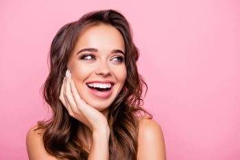 A woman smiling and showing her teeth with a pink background.